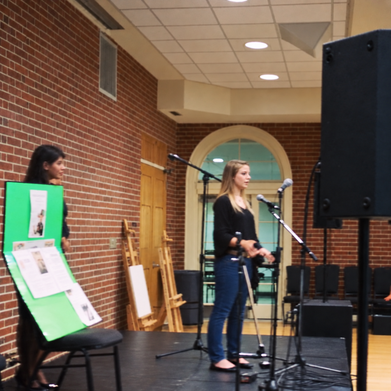 Kasha speaking at microphones in a brick-walled room